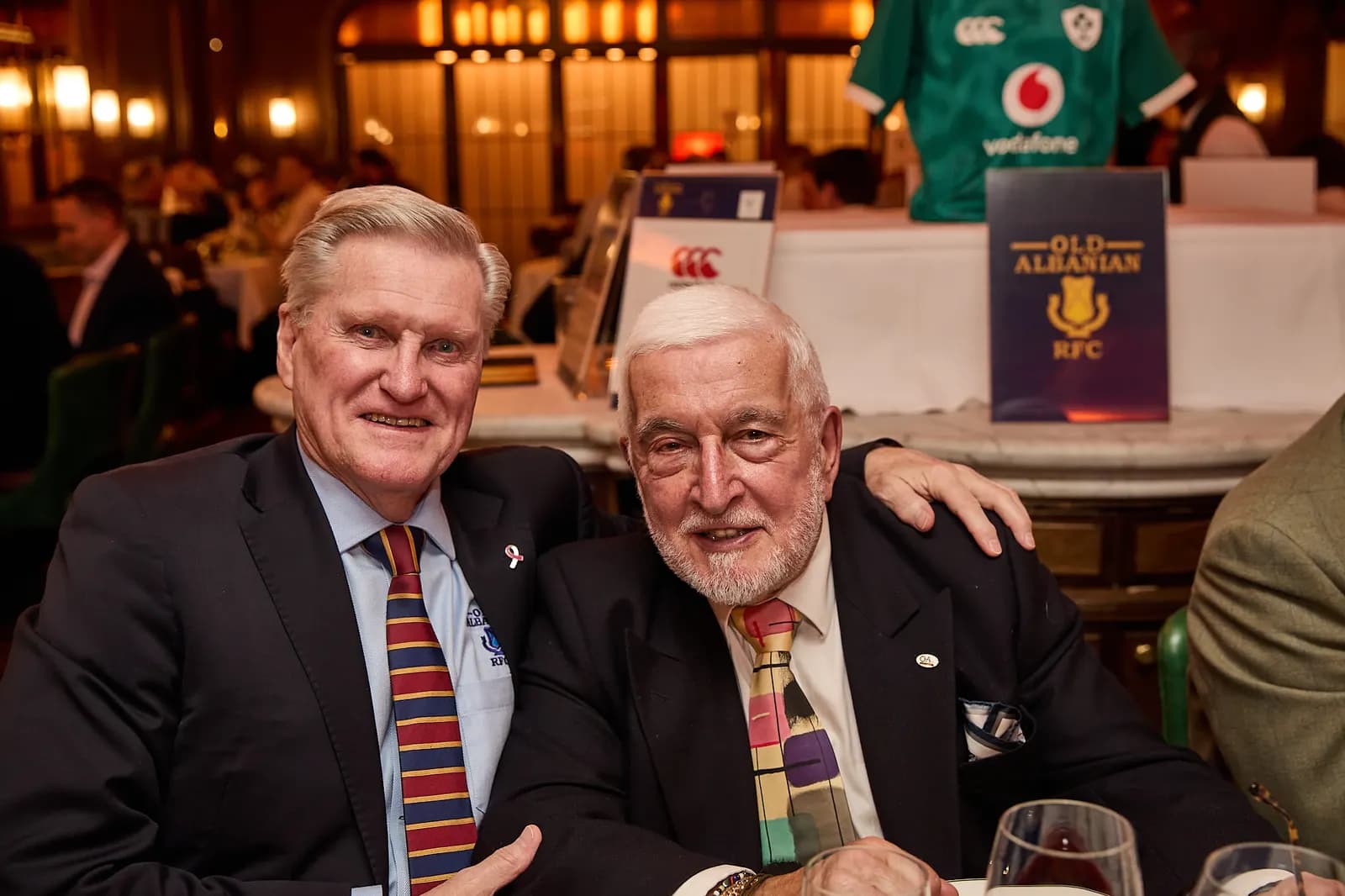 Two guests seated beside the Old Albanian RFC auction display